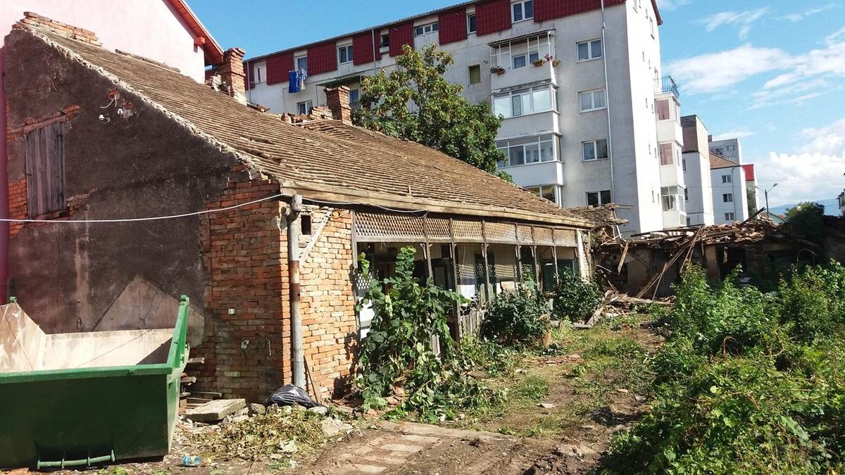 Antes: casa de ladrillo de una planta con tejado de teja y porche, con contenedor de escombros verde