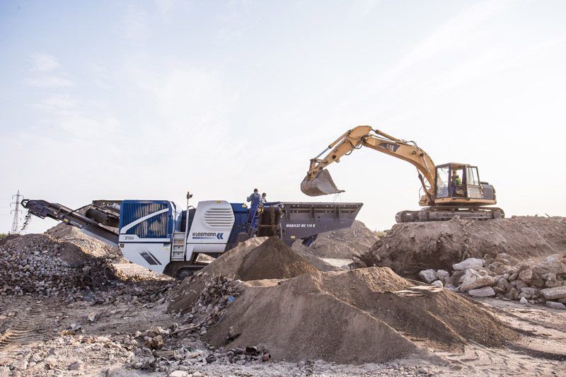 Kleemann Mobicat MC 110 R EVO mobile jaw crusher processing demolition rubble, fed by a CAT excavator