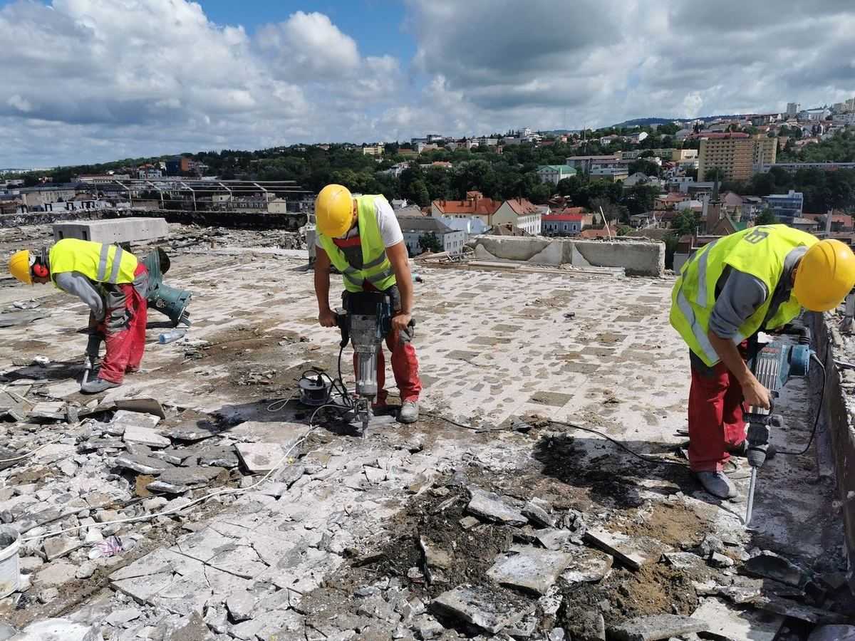 Tres operarios con martillos eléctricos demoliendo las capas de una cubierta plana